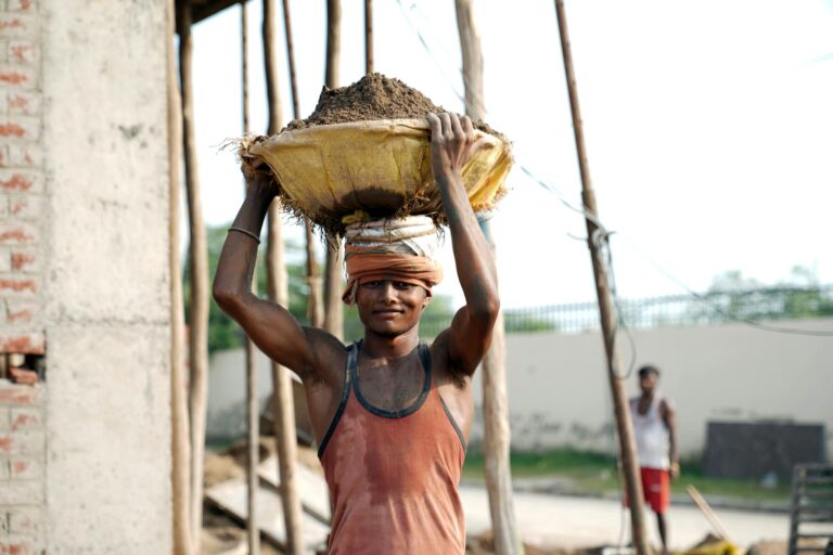 A smiling construction worker carrying a bowl of sand at a building site outdoors.